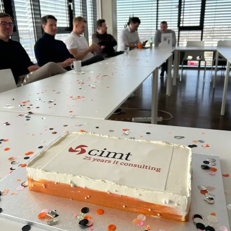 Jubileumtaart met het cimt-logo op een tafel met confetti